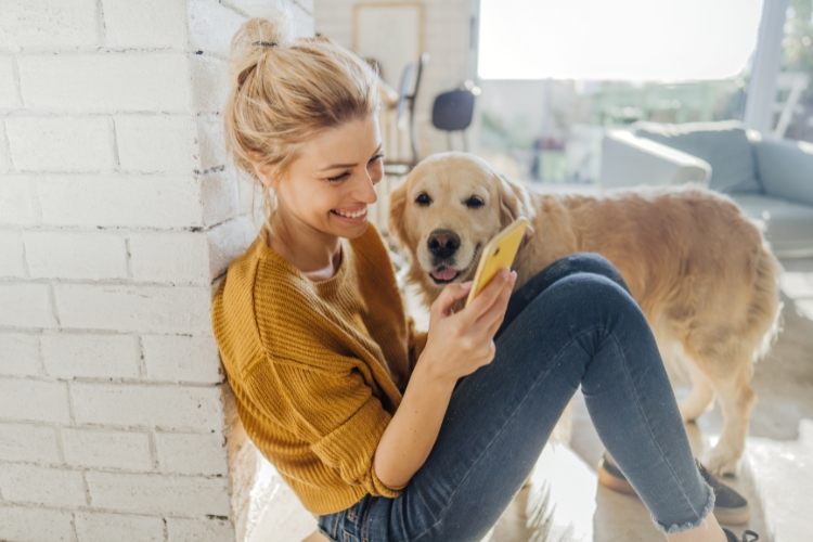 A woman on her phone with her dog by her side